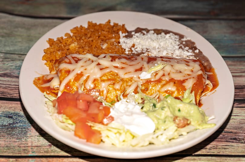 A cheese-covered burrito with rice, refried beans, lettuce, tomatoes, sour cream, and guacamole.