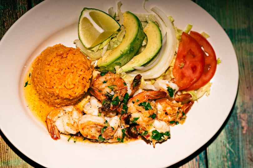 A plate of shrimp scampi with rice, sliced avocado, lime, and tomatoes.