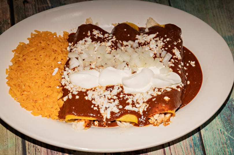 Chicken enchiladas with mole sauce, rice, cotija cheese, diced onions, and sour cream.